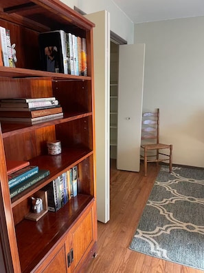Una habitació amb una biblioteca de fusta plena de llibres, una porta blanca, una cadira de fusta i una catifa amb dibuixos al terra.