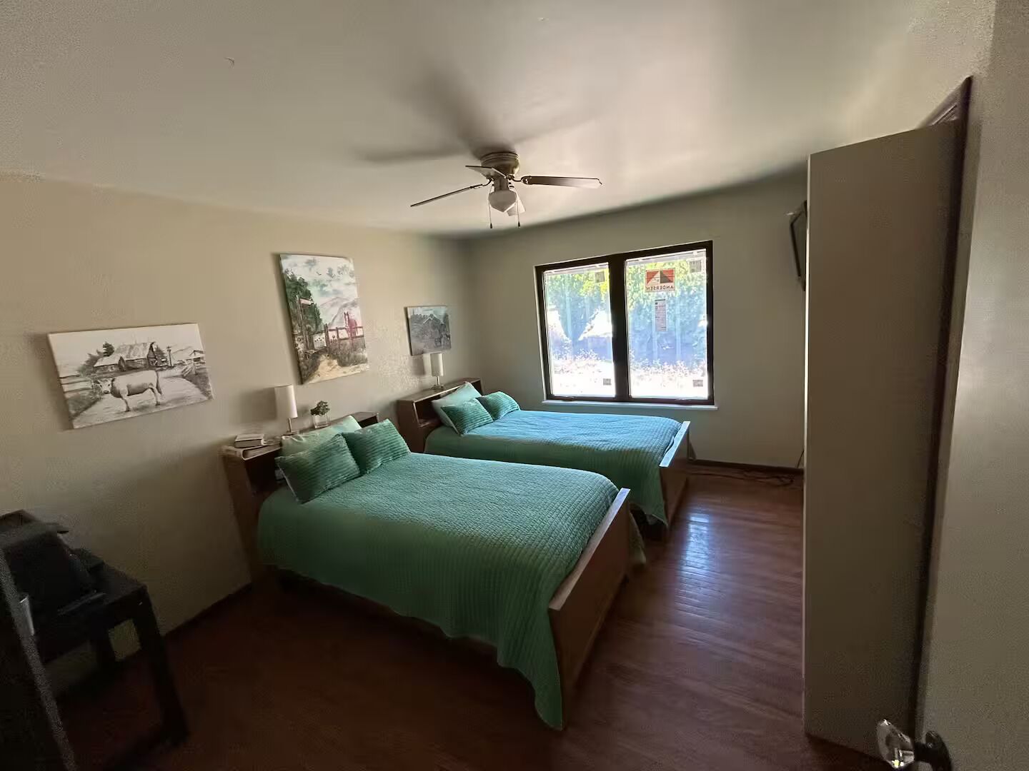 A room with two beds, a ceiling fan, and artwork on the walls.
