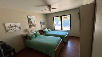 A room with two beds, a ceiling fan, and artwork on the walls.