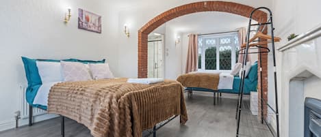 Ein Schlafzimmer mit zwei Betten, einem Ziegelbogen, einem Fenster mit Vorhängen und einem Hängekorbsessel.