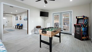 A room with a foosball table, a ceiling fan, a television, and a Mortal Kombat arcade game. - Spacious 5-bedroom house fully Furnished Private Pool – Extended Stays Welcome (Scottsdale)