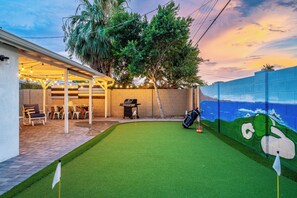 A backyard with artificial turf, a barbecue grill, outdoor seating, and a mural on the wall. - Spacious 5-bedroom house fully Furnished Private Pool – Extended Stays Welcome (Scottsdale)