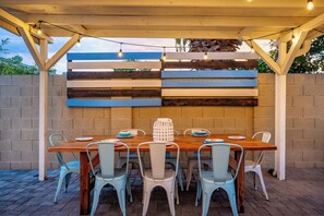 An outdoor patio with a wooden table and chairs, a brick wall, and a pergola with string lights. - Spacious 5-bedroom house fully Furnished Private Pool – Extended Stays Welcome (Scottsdale)