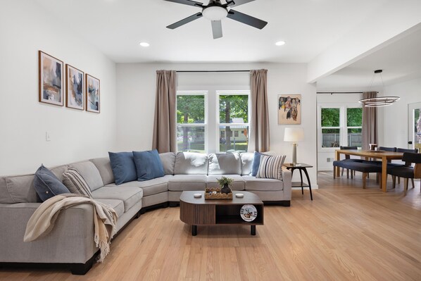 A modern living room with a sectional sofa, a coffee table, and a dining area with a table and chairs.