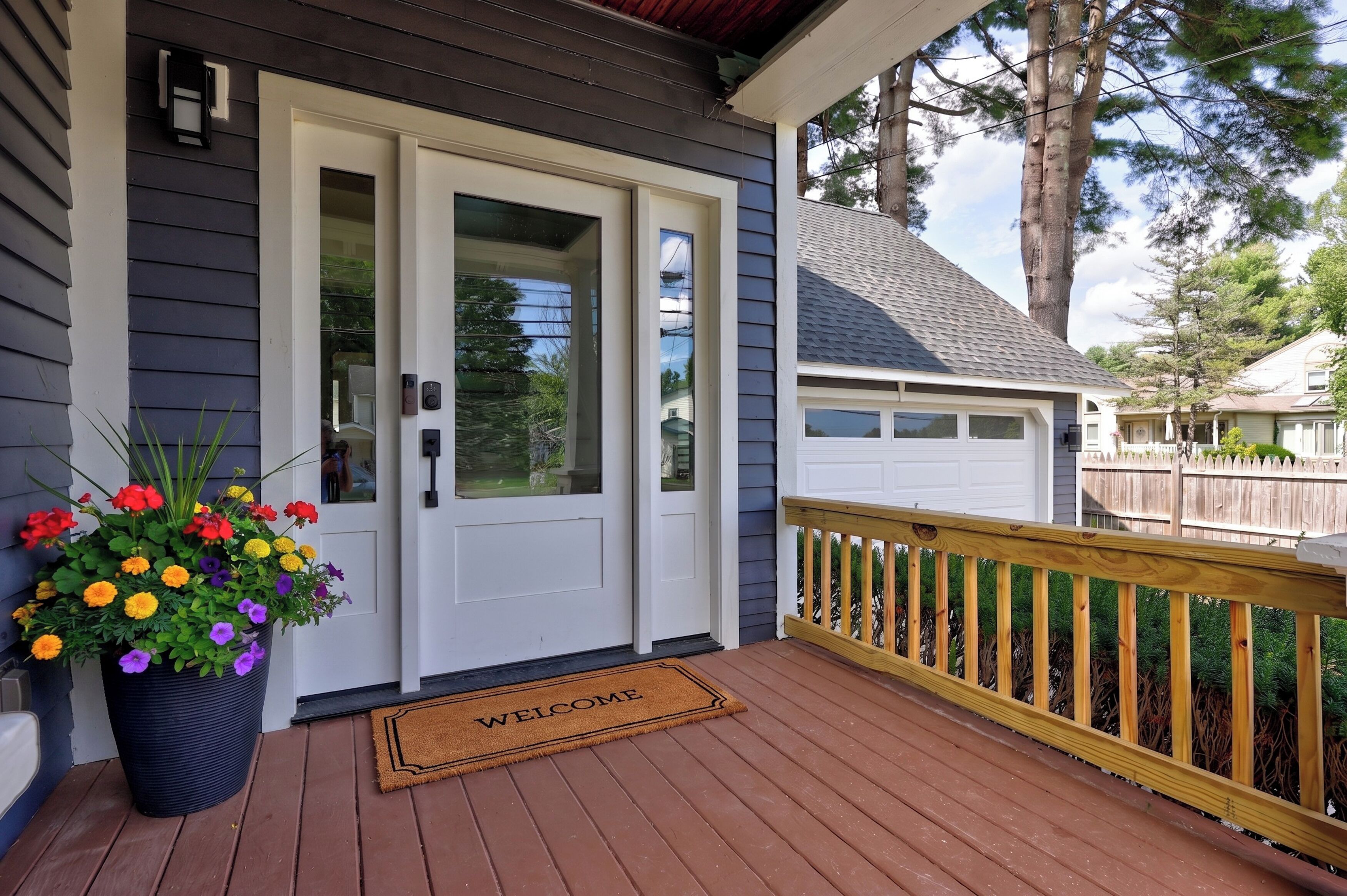 A residential entryway with a white door, a welcome mat, and a potted plant with flowers.
