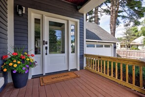 A residential entryway with a white door, a welcome mat, and a potted plant with flowers.