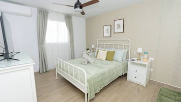 Un dormitorio con cama, mesitas de noche, ventilador de techo y ventana con cortinas.