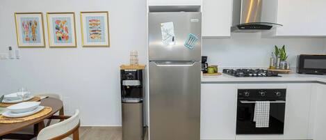 Et lille køkken med køleskab, komfur, mikrobølgeovn og en vanddispenser.