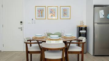 Ein Essbereich mit einem Tisch, gedeckt für vier Personen, umgeben von Holzstühlen mit gepolsterten Sitzen. An der Wand über dem Tisch hängen drei gerahmte Kunstwerke.