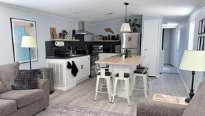 A modern kitchen with a central island, white cabinetry, and a dining area with bar stools. - Angler’s Hideaway: Your Peaceful Escape for Fishing, Fun & Relaxation (Homosassa)