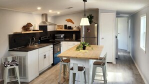 A modern kitchen with a central island, white cabinetry, and a dining area with a wooden table and chairs. - Angler’s Hideaway: Your Peaceful Escape for Fishing, Fun & Relaxation (Homosassa)