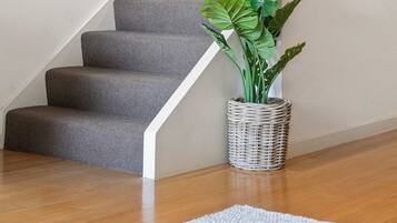 A staircase with grey carpeted steps, a metal handrail, a clock on the wall, and a potted plant with broad leaves.