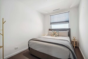 A bedroom with a bed, a window, a bedside table, and a lamp.