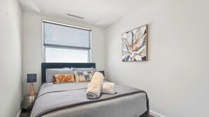 A bedroom with a bed, a window, a painting, and a nightstand with a lamp. - Arcady, Norwood Townhouse Near The Parade and City (Norwood)