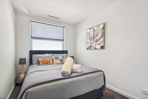 Ein Schlafzimmer mit einem Bett, einem Fenster, einem Bild und einem Nachttisch mit einer Lampe.