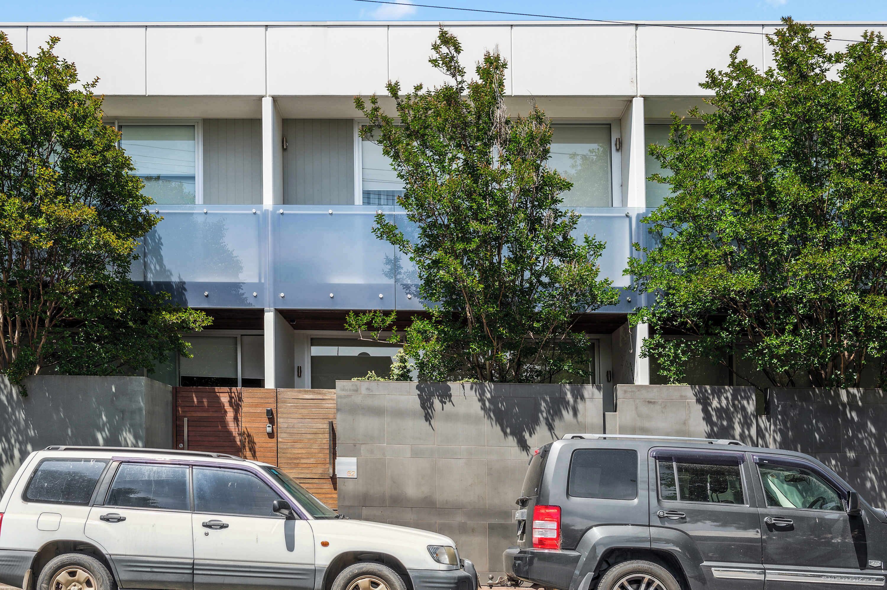 A modern two-story building with a flat roof, large windows, and a covered outdoor area.