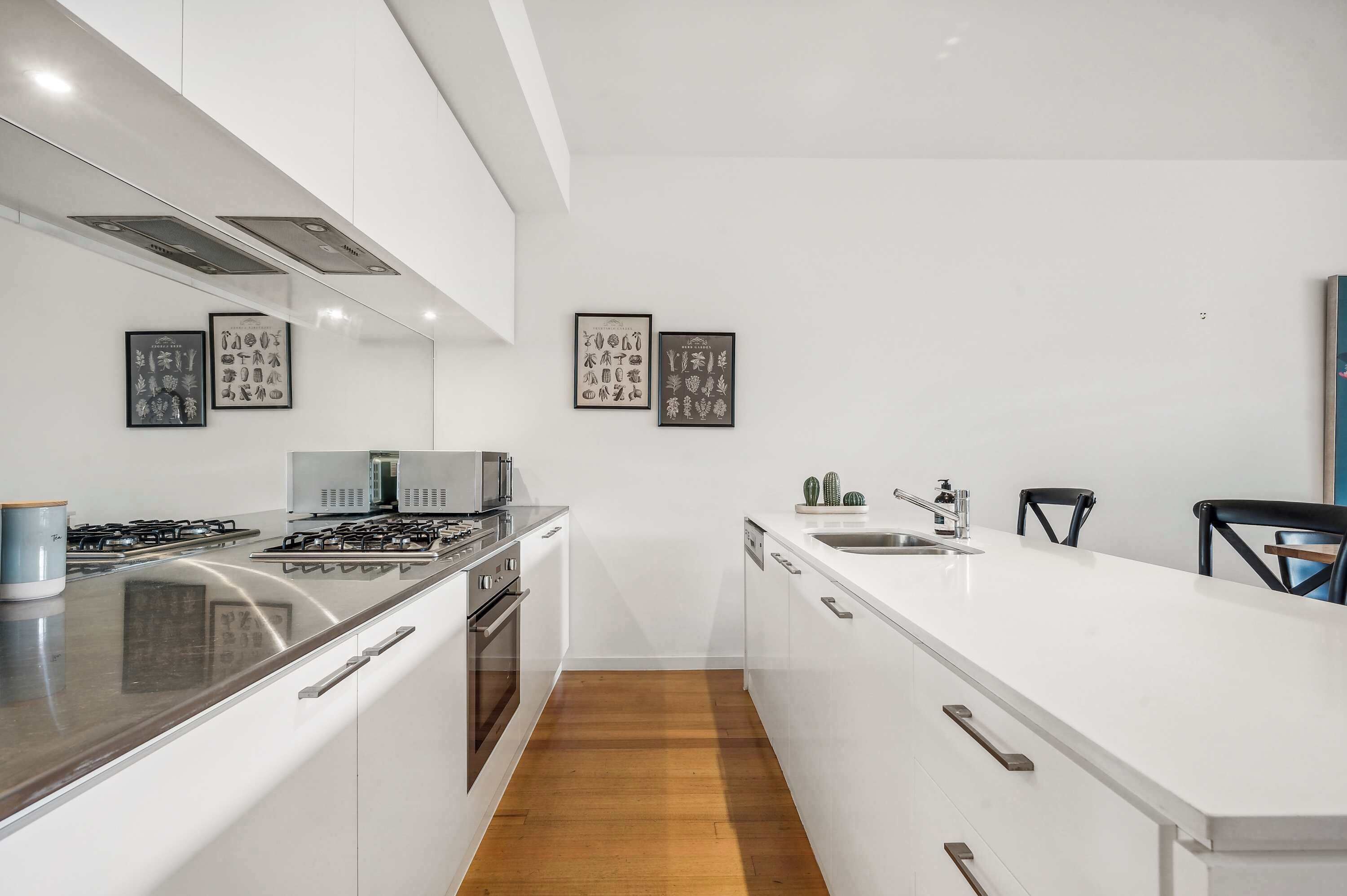 A modern kitchen with a central island, stainless steel appliances, and framed botanical prints on the wall.