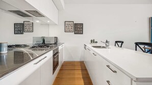 A modern kitchen with a central island, stainless steel appliances, and framed botanical prints on the wall. - Arcady, Norwood Townhouse Near The Parade and City (Norwood)