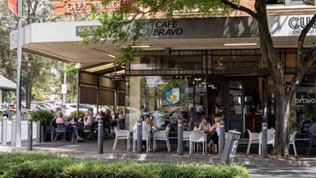 An outdoor cafe with tables and chairs, a covered seating area, and a building with a cafe sign.