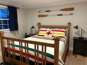 Ein Schlafzimmer mit einem hölzernen Bett, einem Nachttisch, einer Lampe und einem Fenster mit Vorhängen.