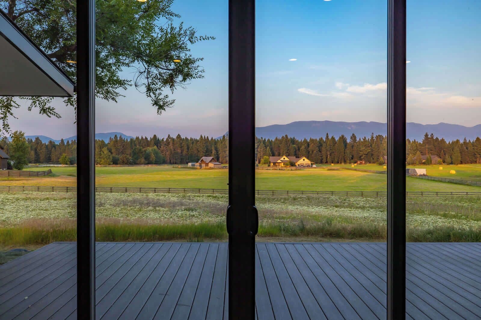 A view from a room with large windows overlooking a rural landscape with fields, trees, and distant mountains.