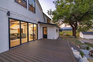 A modern house with a wooden deck, large sliding glass doors leading to a living area, and a view of the countryside. - The Willow House - Hot Tub w/ Views near Glacier (Columbia Falls)