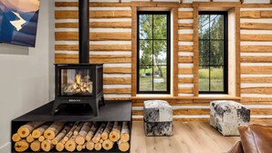 Ein Holzblockhaus-Interieur mit Kaminofen, einem Fenster mit Blick ins Freie und einem Holzstapel.
