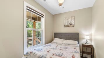 A bedroom with a bed, a nightstand, a lamp, a window with blinds, and a wall-mounted artwork.