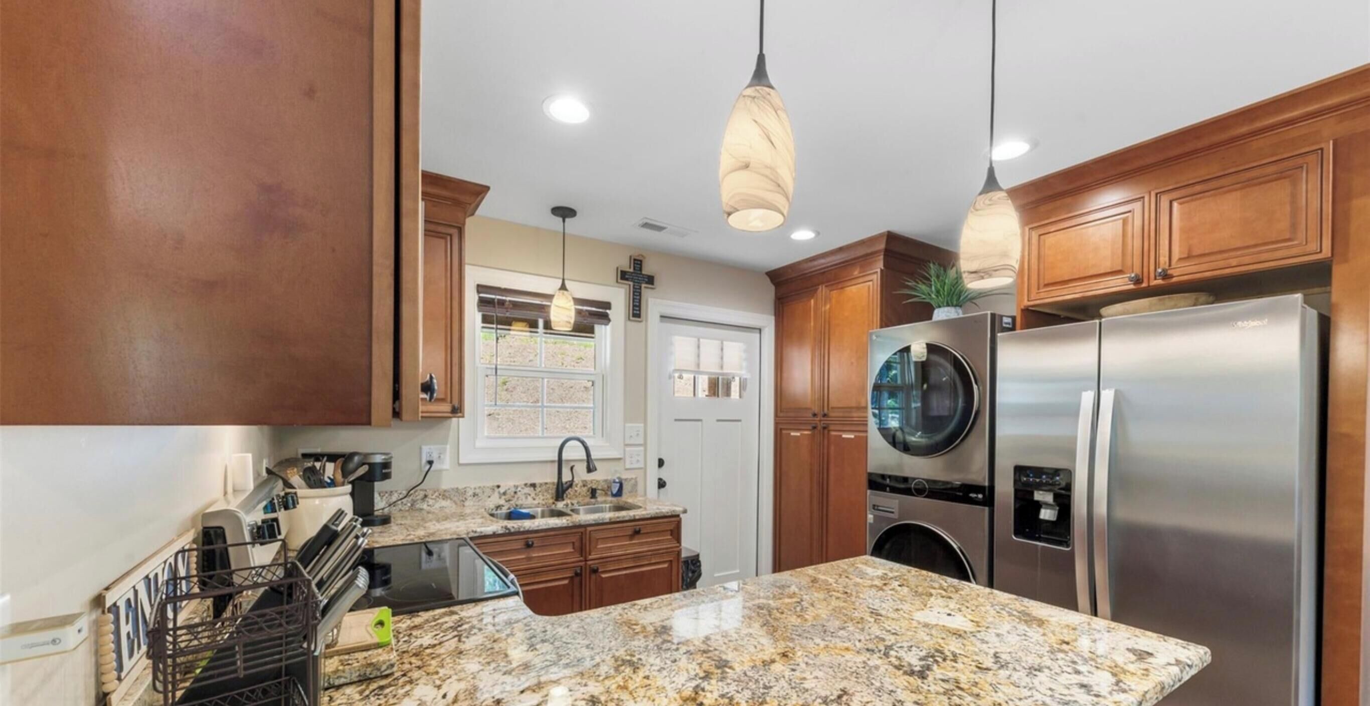 A kitchen with granite countertops, stainless steel appliances, wooden cabinets, and pendant lighting.