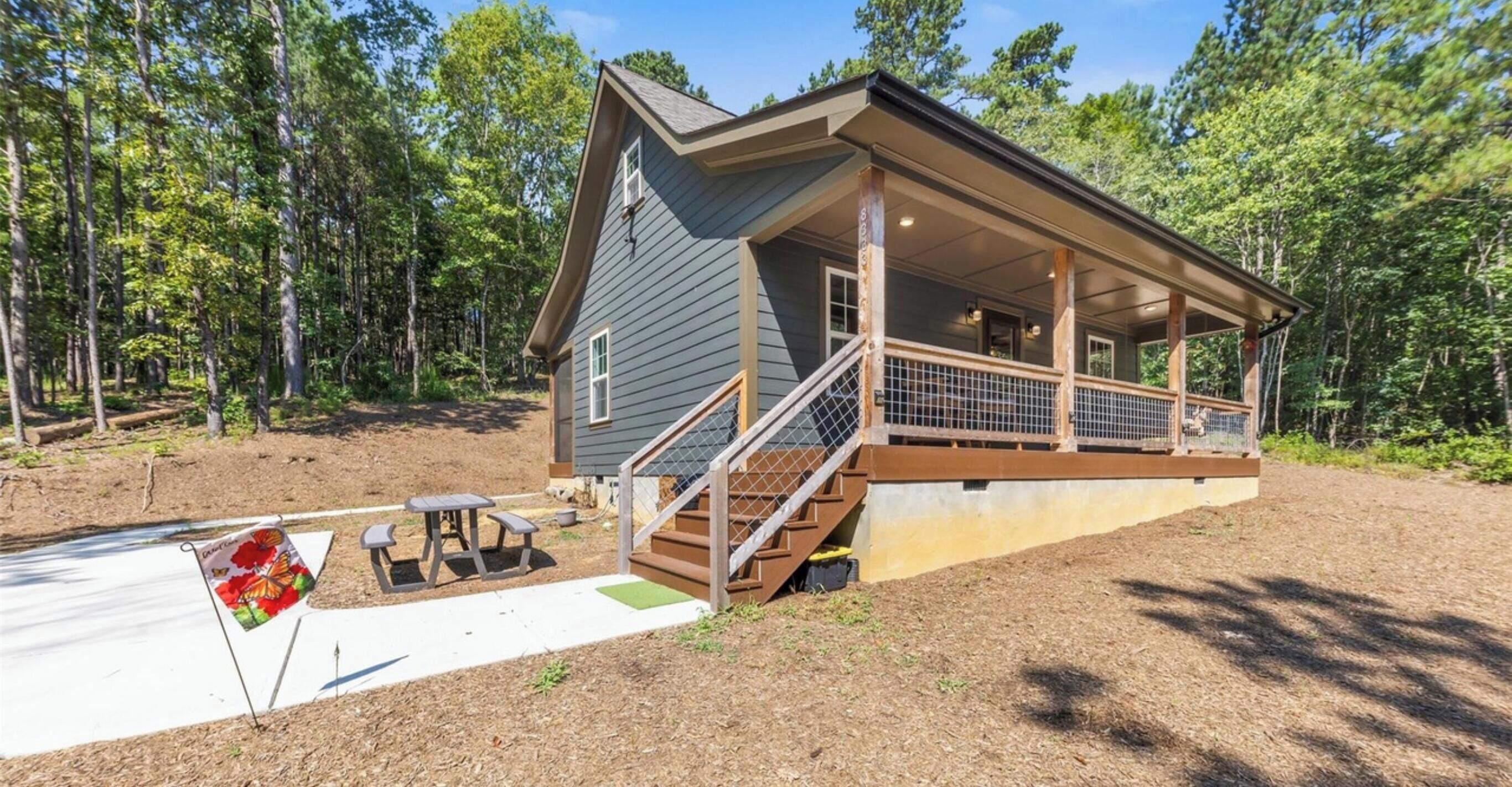A cabin with a covered porch, a small outdoor seating area, and a flag.