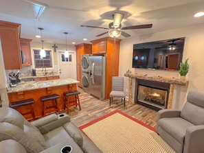 A modern kitchen with a central island, bar stools, a fireplace, and a ceiling fan.