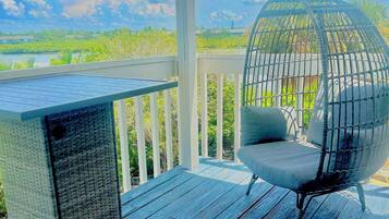 A deck with a woven chair and a table, overlooking a body of water and greenery.