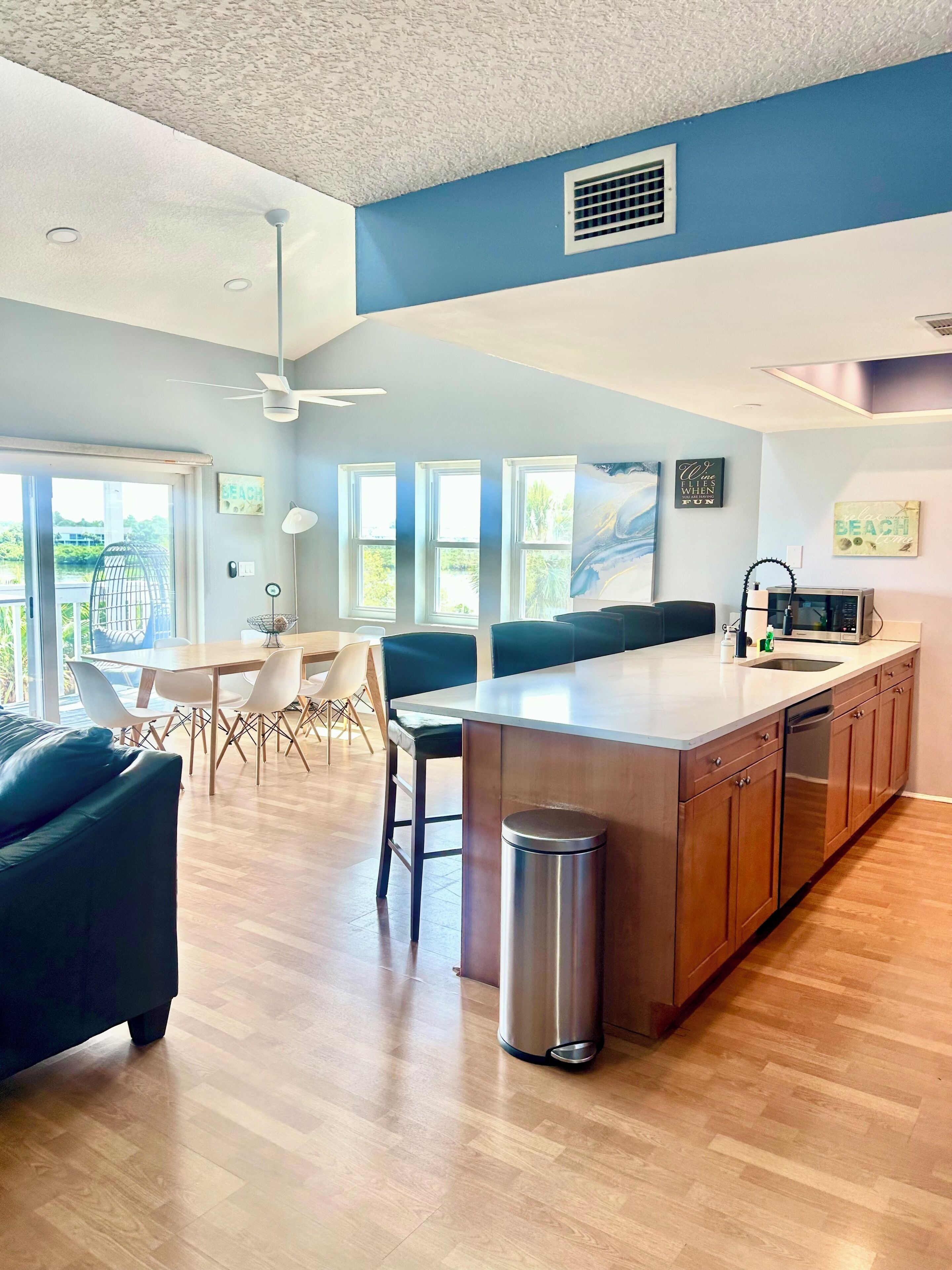 A modern kitchen with a central island, wooden cabinets, and a stainless steel trash can.