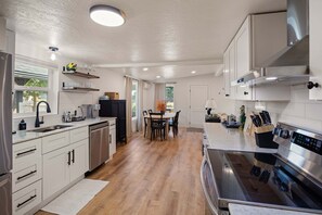 Une cuisine moderne dotée d’appareils électroménagers en acier inoxydable, un coin repas avec une table et des chaises, et une vue sur l’extérieur par la fenêtre.