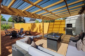 An outdoor patio with a covered seating area, a grill, and a fire pit.