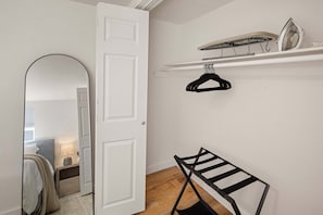 Une pièce avec une porte blanche, un miroir, un portant à vêtements et une étagère avec un fer à repasser.