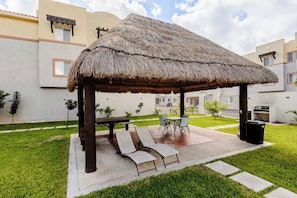 A covered outdoor seating area with a thatched roof, a table, and lounge chairs. - Your peaceful retreat in Playa del Carmen (Playa del Carmen)