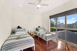 Ein Schlafzimmer mit zwei Einzelbetten, einem Deckenventilator und einem großen Fenster mit Blick auf ein Dach.