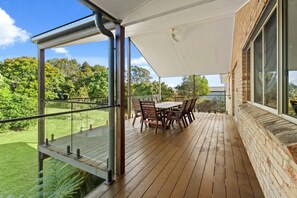 En overdækket terrasse med et bord og stole, med udsigt over en frodig have.