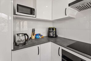 Eine moderne Küche mit weißen Schränken, einer Mikrowelle, einer Kaffeemaschine und einem Wasserkocher.