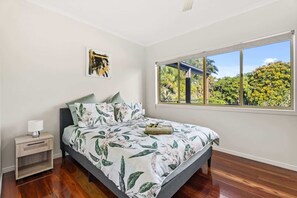 Ein Schlafzimmer mit einem Bett, einem Nachttisch, einem Fenster mit Blick auf Bäume und einem Bild an der Wand.