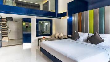 A modern bedroom with a large bed, a seating area, and a glass wall.