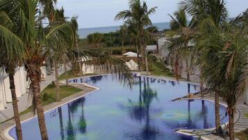 A large, curved swimming pool surrounded by palm trees and a view of the ocean.