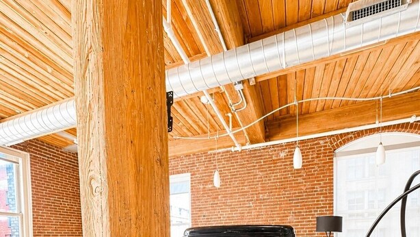 Une machine à café DeLonghi et un grille-pain sont posés sur un plan de travail dans une cuisine moderne, dont l’intérieur est caractérisé par des poutres en bois apparentes et des murs en briques.