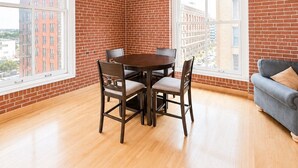 A room with a brick wall, wooden ceiling, a dining table with chairs, and a sofa.