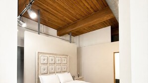 A bedroom with a wooden ceiling, a bed with a headboard, a bedside table, and a nightstand.