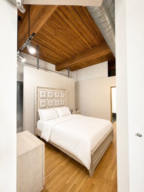 A bedroom with a wooden ceiling, a bed with a headboard, a bedside table, and a nightstand.