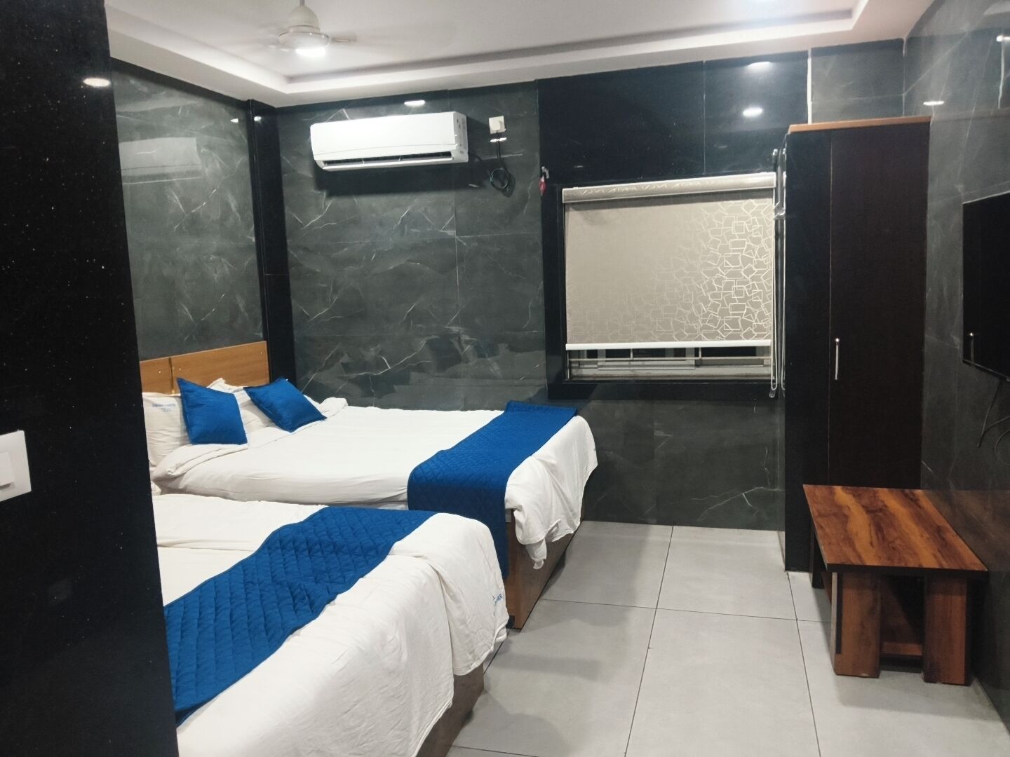 A hotel room with two beds, a bench, a wardrobe, and an air conditioning unit.