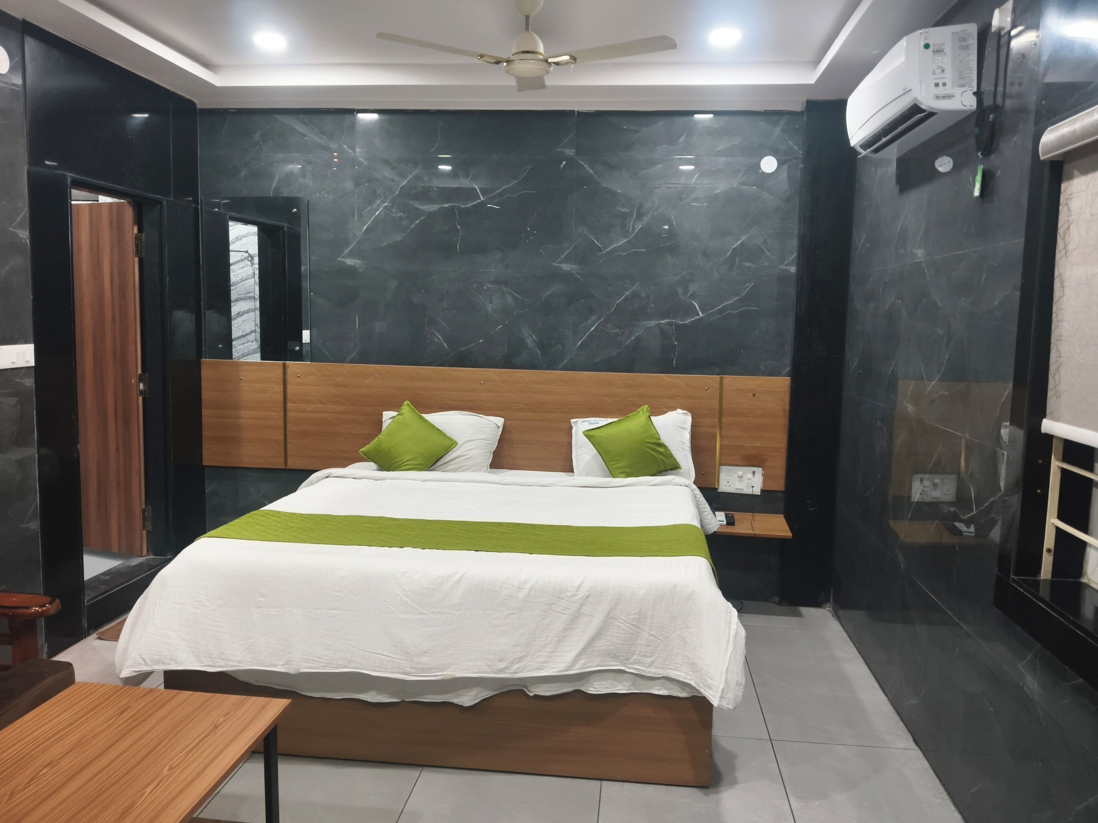 A modern hotel room with a bed, bedside tables, a ceiling fan, and an air conditioning unit.