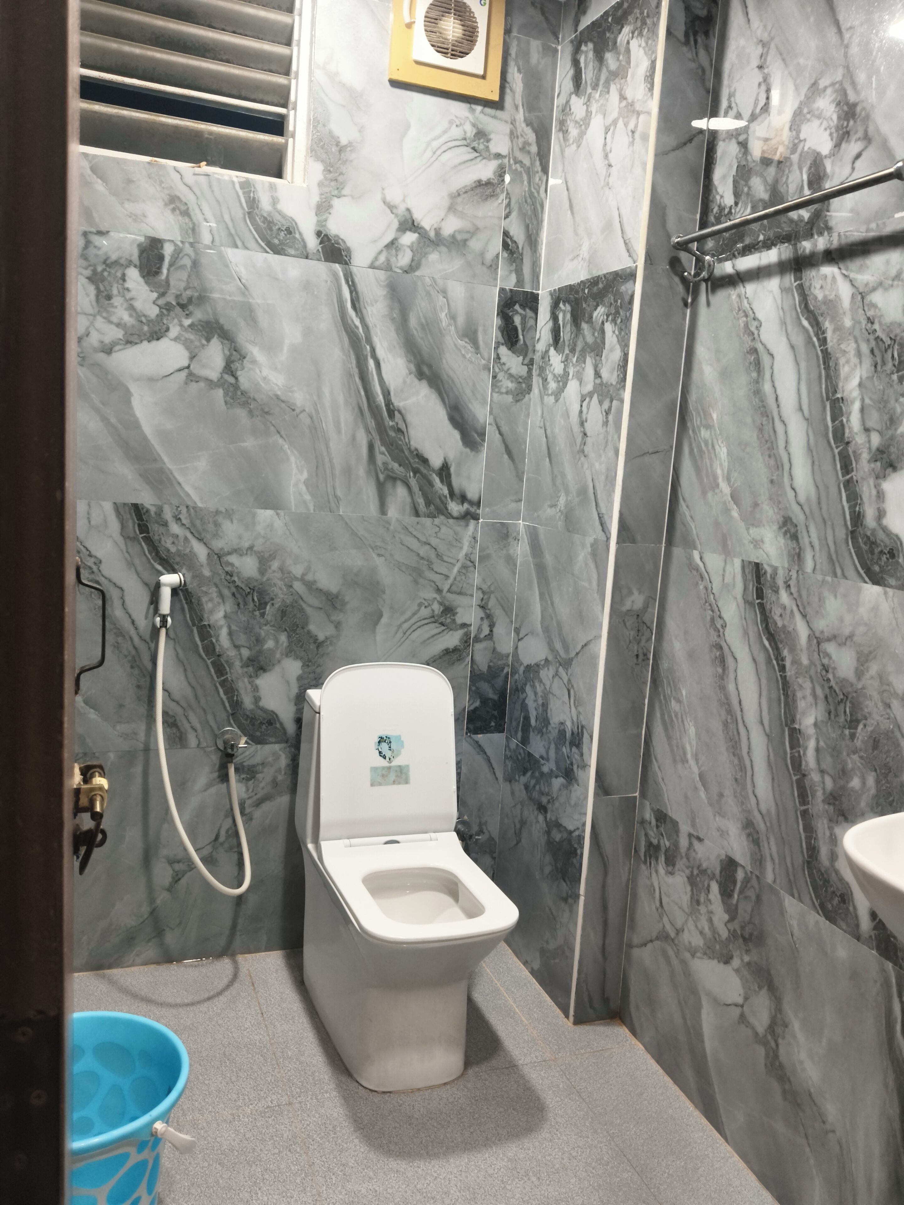 A bathroom with a toilet, shower, and sink against marble walls.